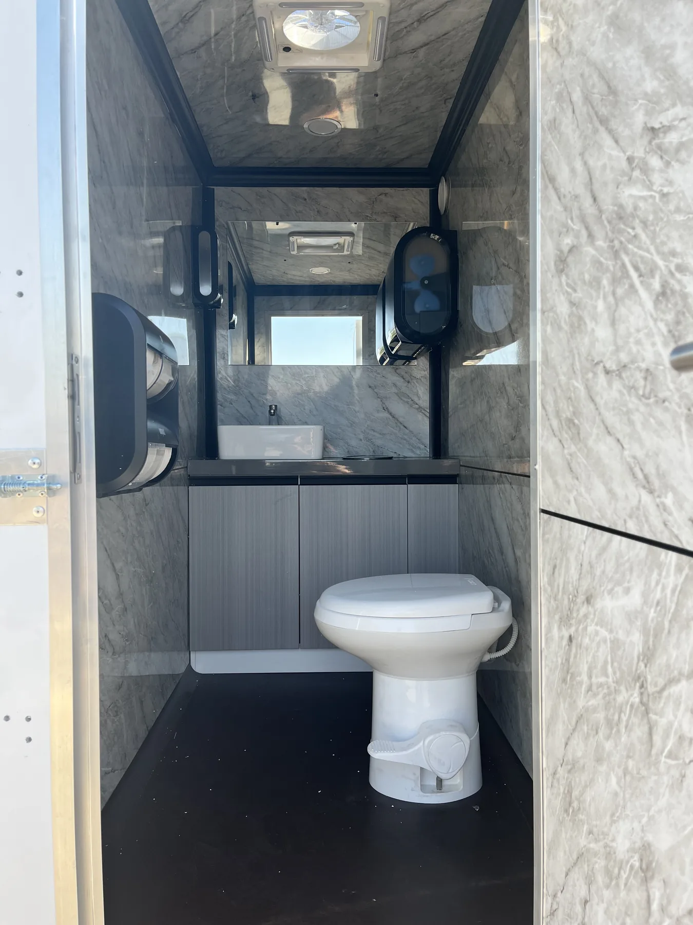 Lux Loos trailer interior with marble-look walls, ceramic vessel sink and flushing toilet